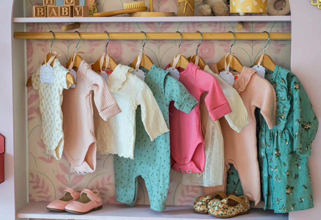 Deretan baju bayi baru lahir digantung di rak dengan sepatu kecil di bawahnya
