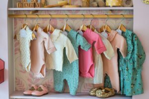 Deretan baju bayi baru lahir digantung di rak dengan sepatu kecil di bawahnya