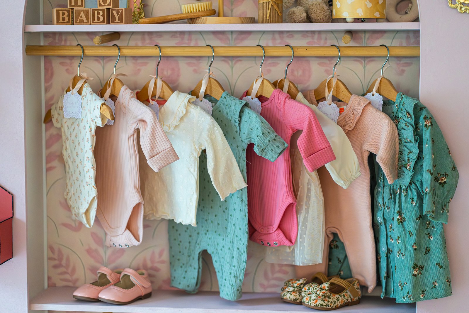 Deretan baju bayi baru lahir digantung di rak dengan sepatu kecil di bawahnya